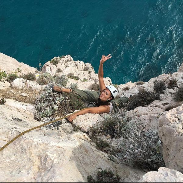 Frau klettert am Fels mit schönen blauem Meer im Hintergrund
