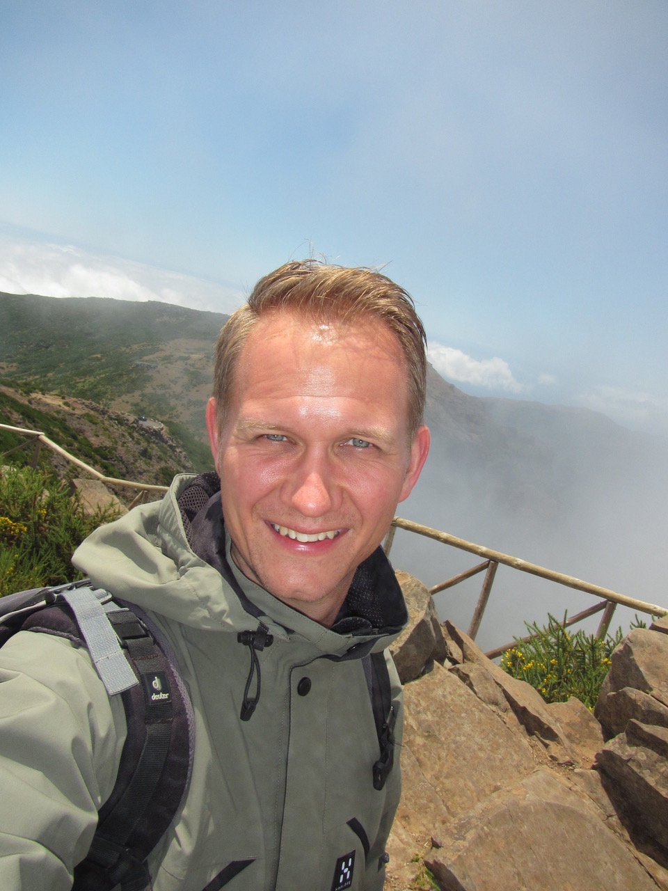 Mann mit Wanderkleidung steht draussen von grossen Felsen umgeben. Er lächelt und die Sonne scheint ihm ins Gesicht